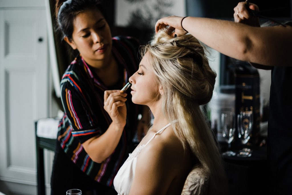Bride has her hair styled whilst having makeup applied.