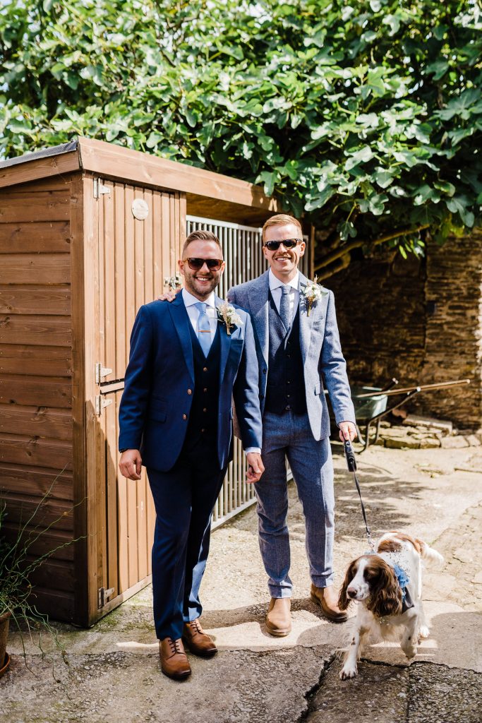 Both grooms smile at the camera with dog.