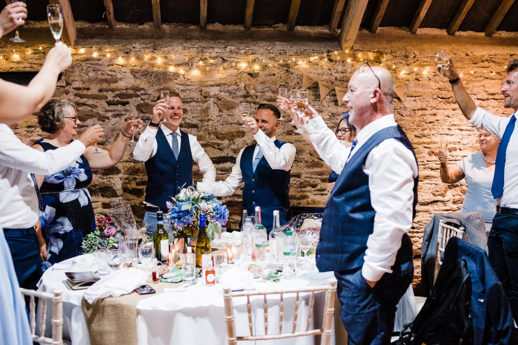 Grooms and family toast in stone barn.