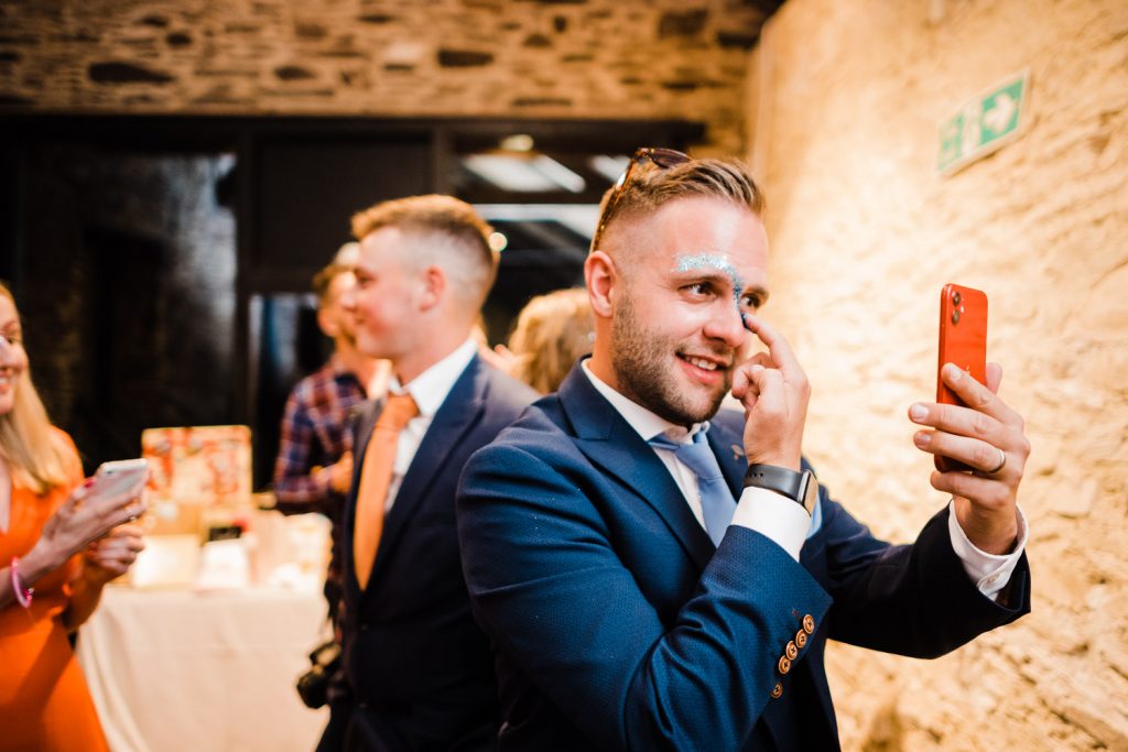 Groom applies glitter to his face using phone.