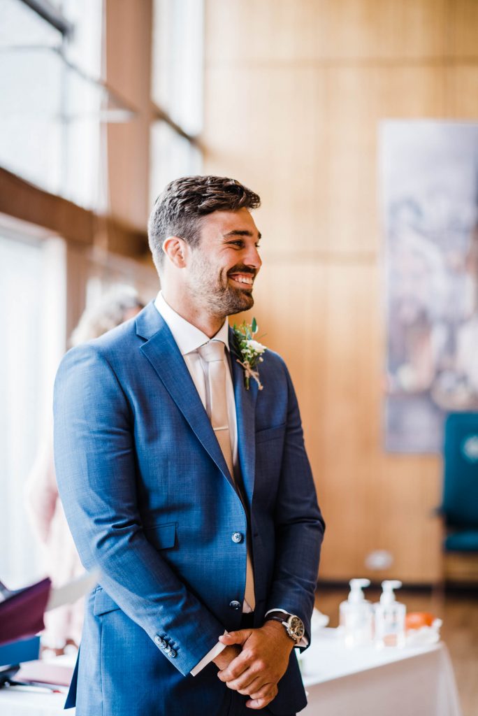 Groom smiles back at his bride as she enters the ceremony room.