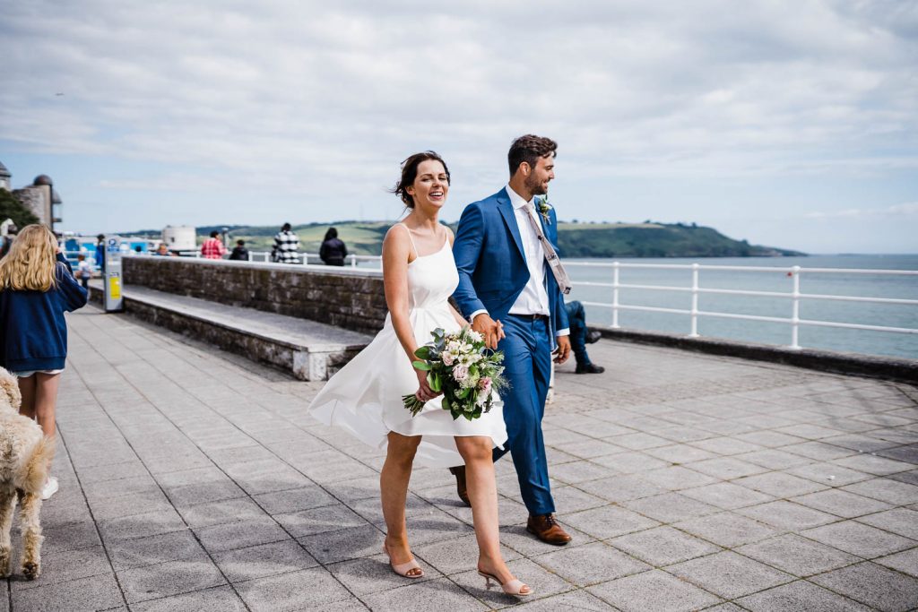 Bride and groom walk hand-in-hand, along the waterfront on Plymouth Hoe.