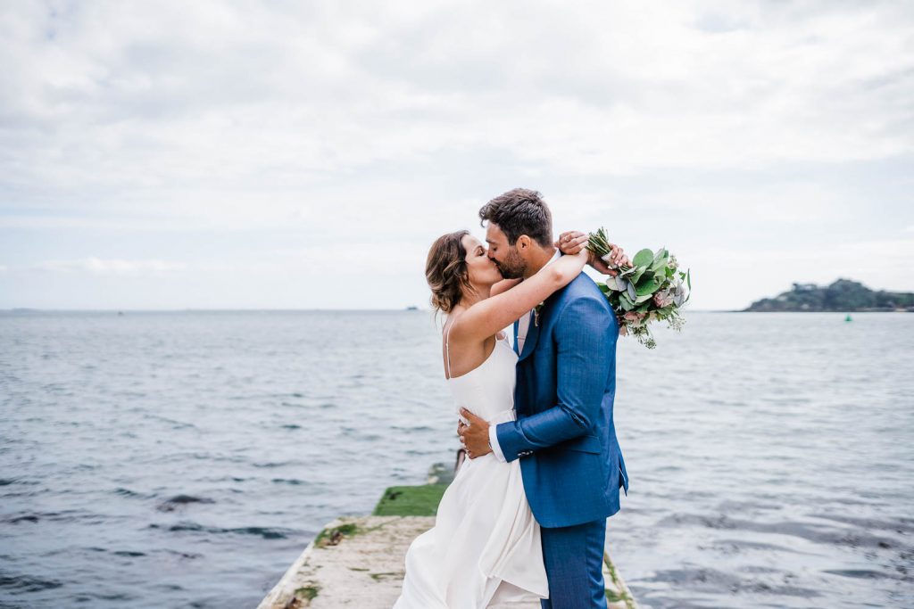 Bride and groom kiss in front of Plymouth Sound and Drakes Island.