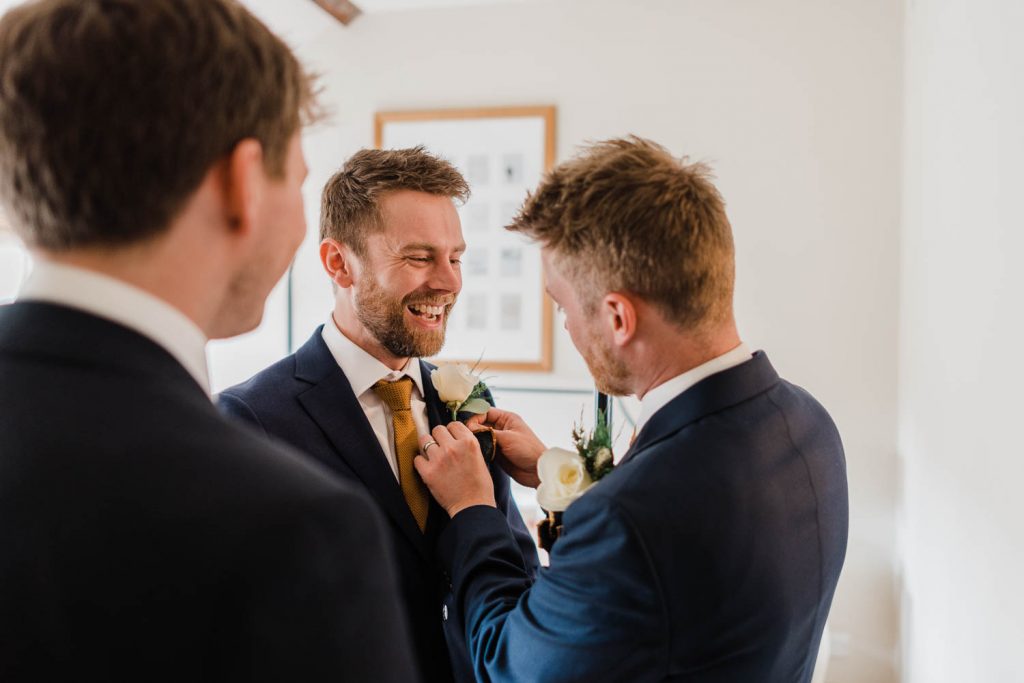 The groom laughs as his brother pins on his boutonniere.