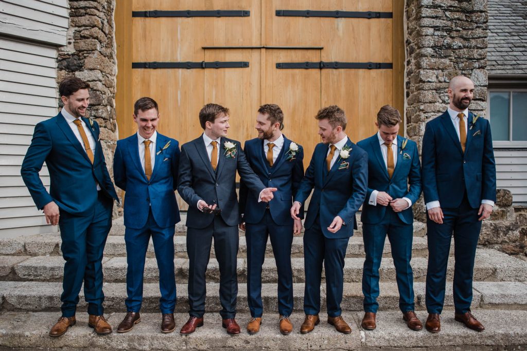 Groom poses for photos with his groomsmen outside the doors of the Great Barn.
