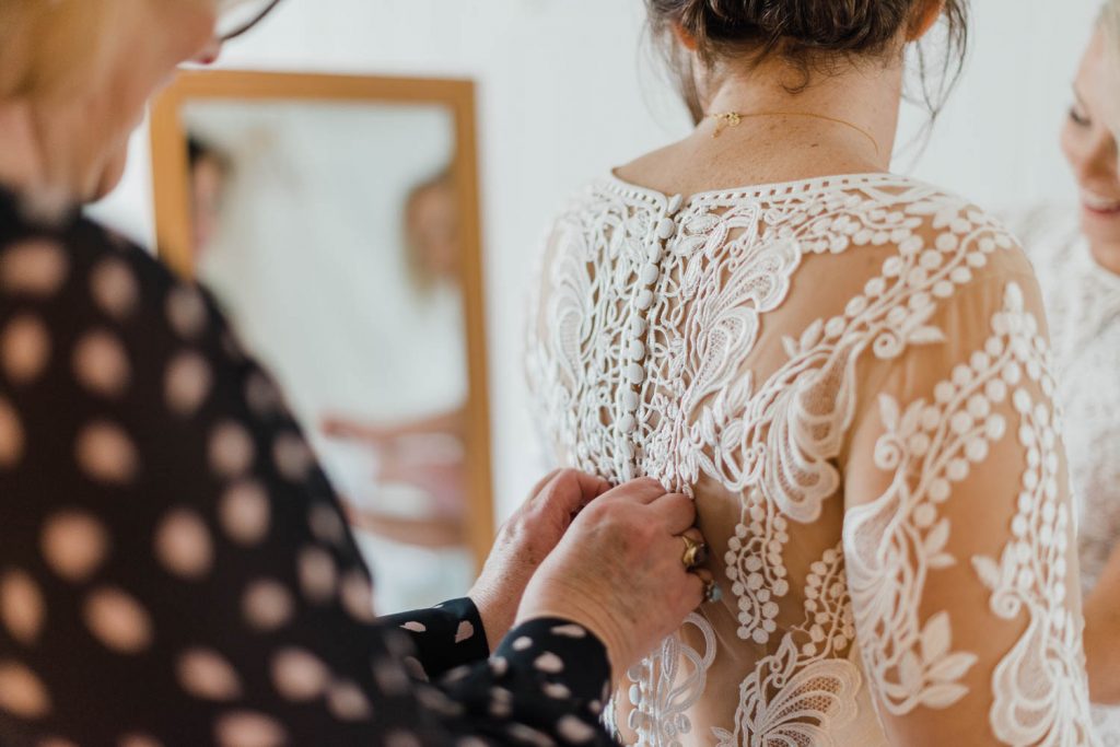The bride's mother fastens the buttons on the back of the bride's dress.