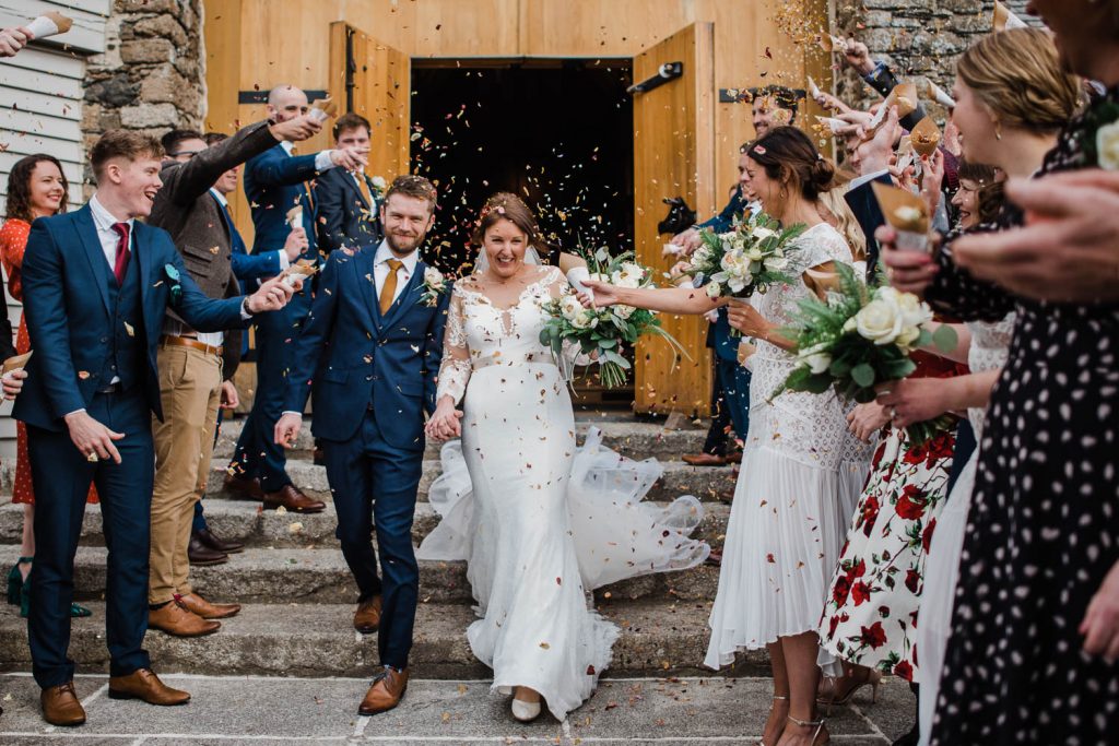 Bride and Groom are showered with confetti on the steps of the Great Barn Devon.