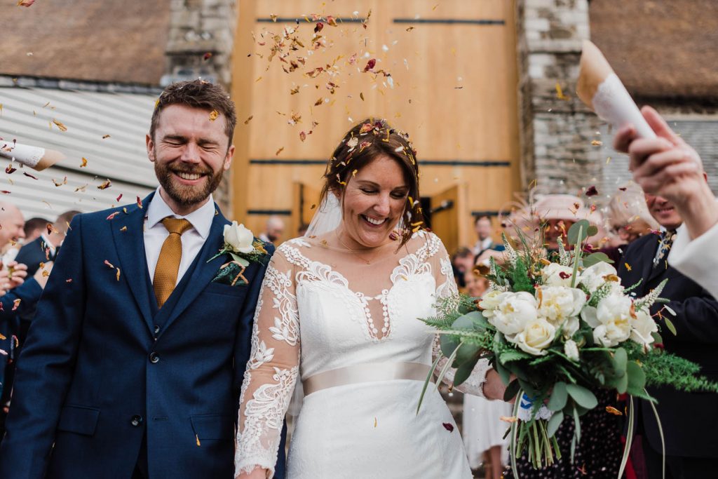 The bride and groom are showered with confetti outside the Great Barn Devon.