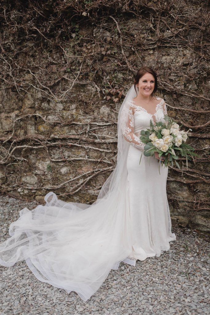 Bride poses infant of stone wall with bridal bouquet.