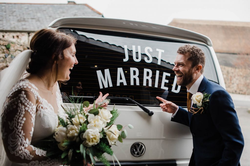 Bride and Groom point to 'Just Married' sign on the back of their van.
