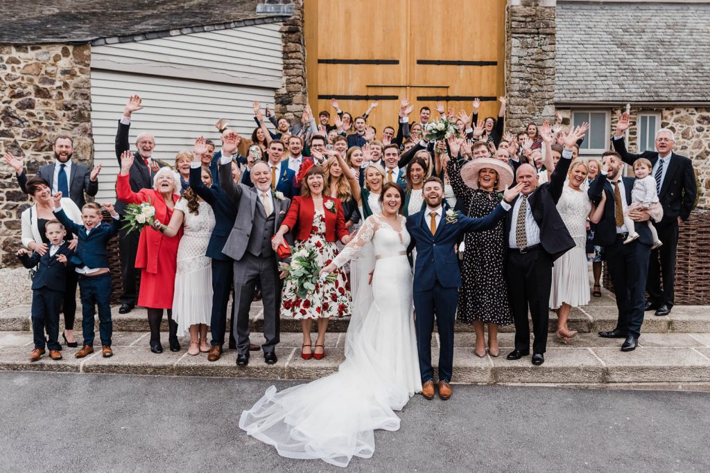 Bride and groom cheer with all their wedding guests outside the Great Barn Devon.