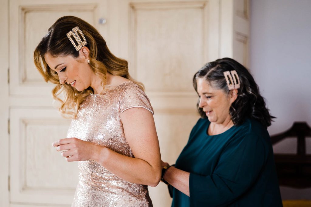 The mother of the bride helps fasten her daughter's dress.