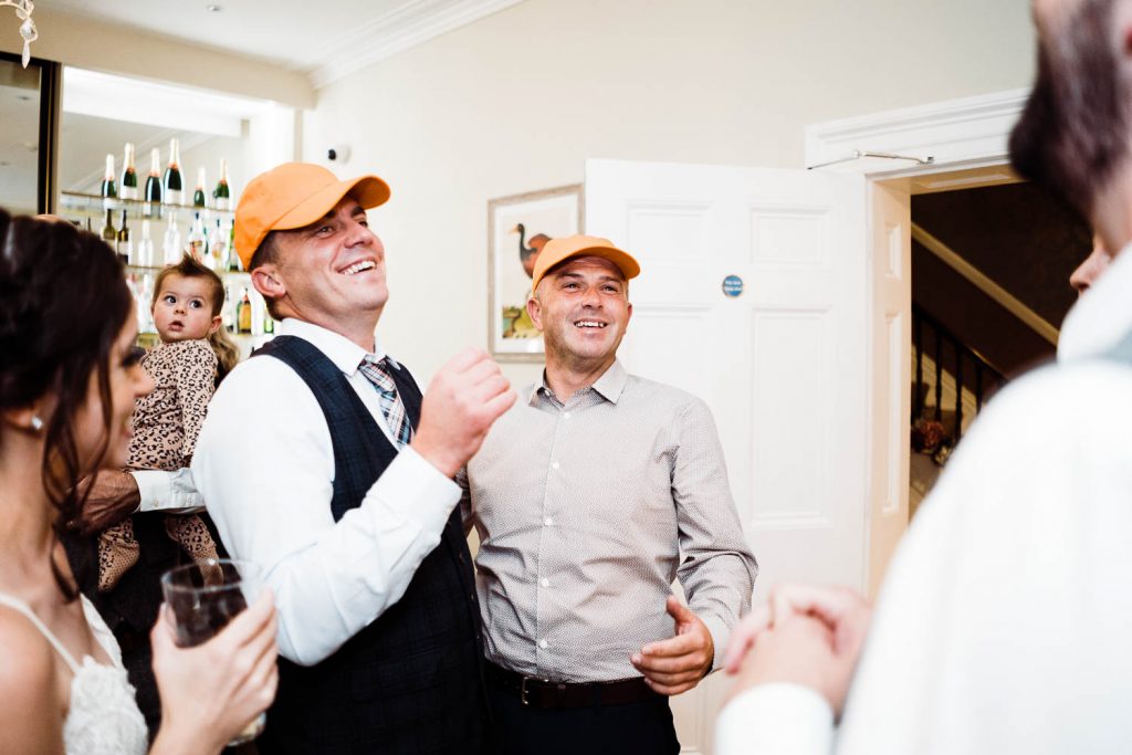 wedding guests laugh wearing orange baseball caps.