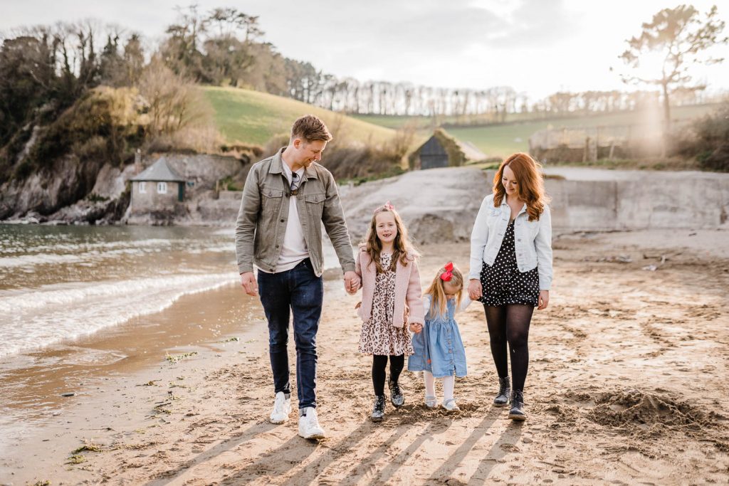 Family of four walk hand in hand on Mothecombe Beach.