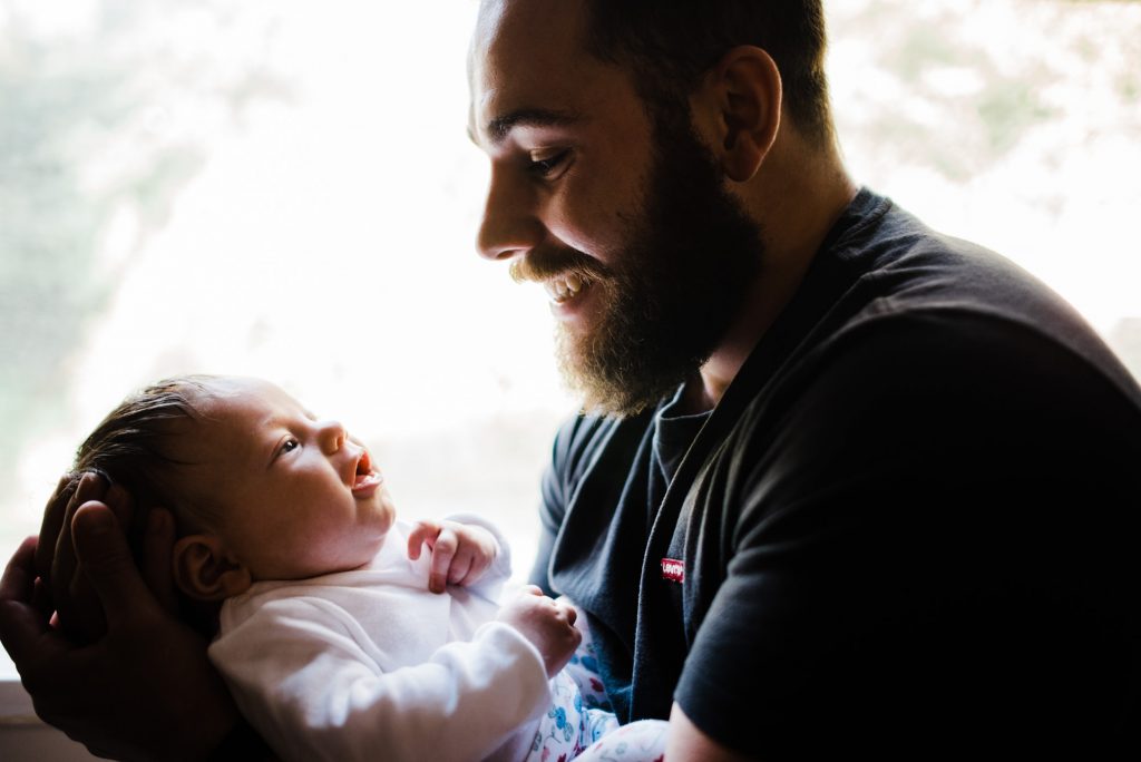 New father holds his baby girl in front of window.