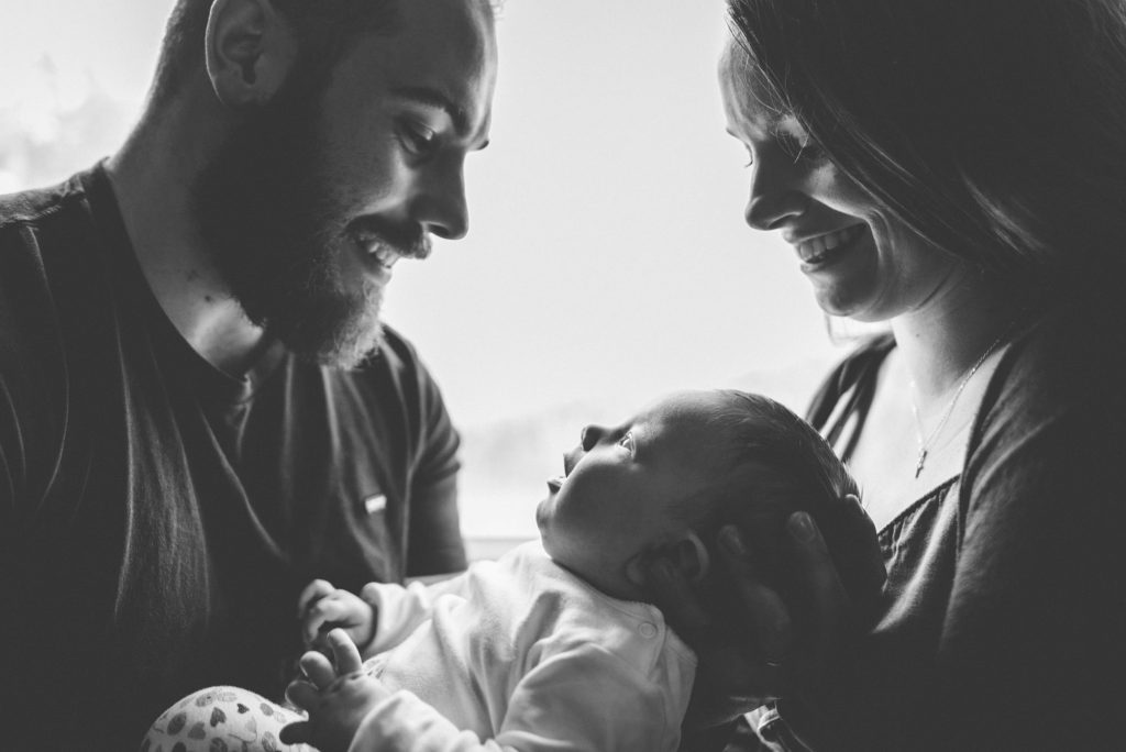mother and father hold their baby daughter in front of window.