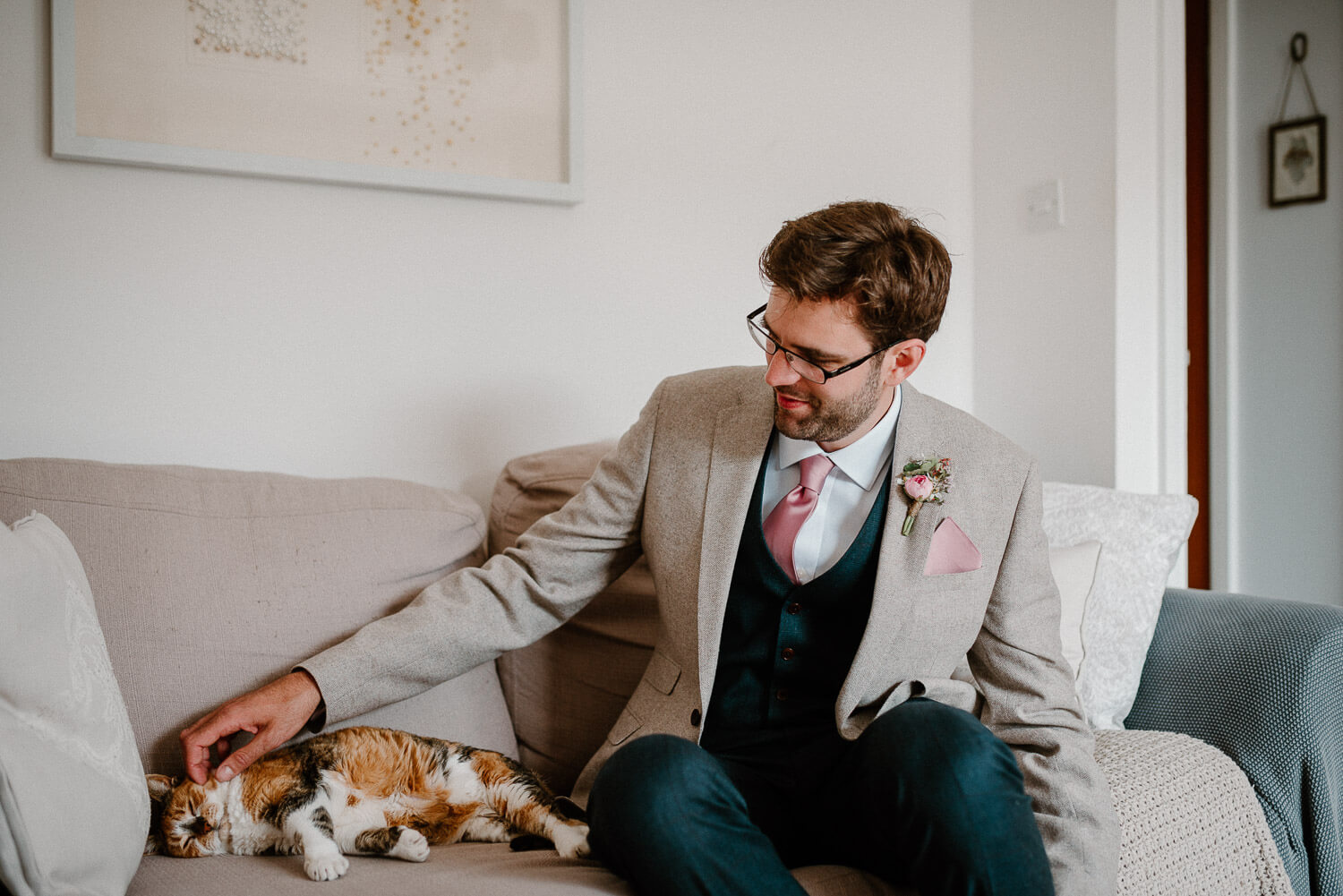 Groom strokes his cat on the sofa ahead of wedding ceremony.