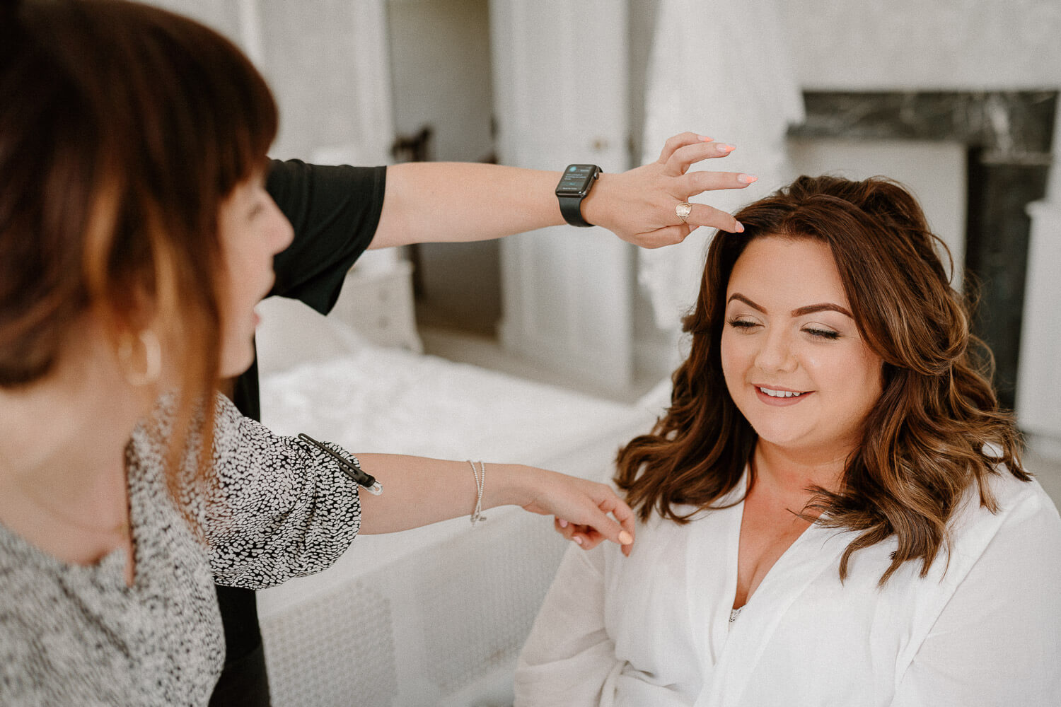 Makeup artist and hair stylist assist bride in preparing for her wedding day.