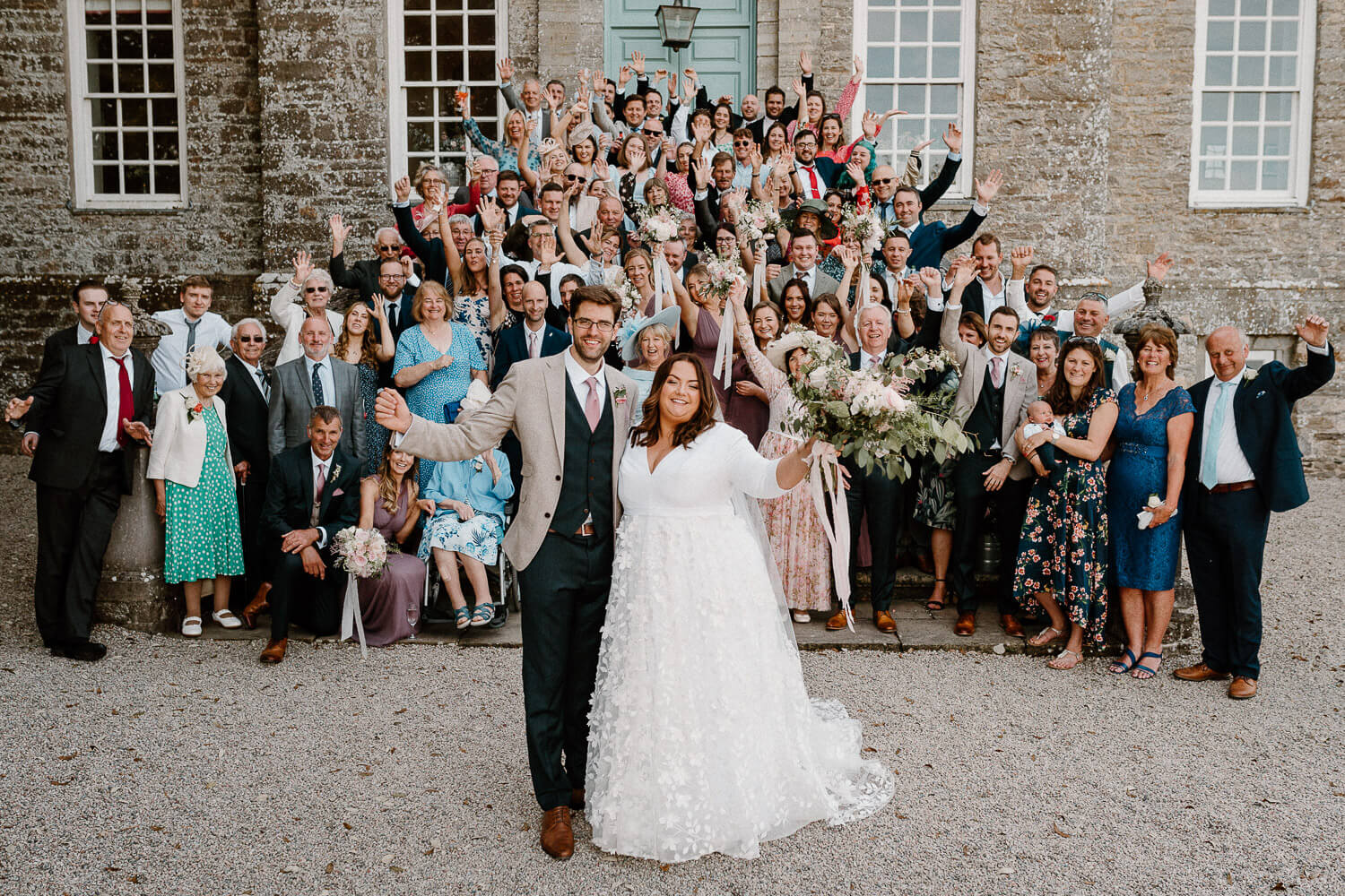 Bride and groom with all their wedding guests pose for a photo on the front steps at Kingston Estate, Devon.