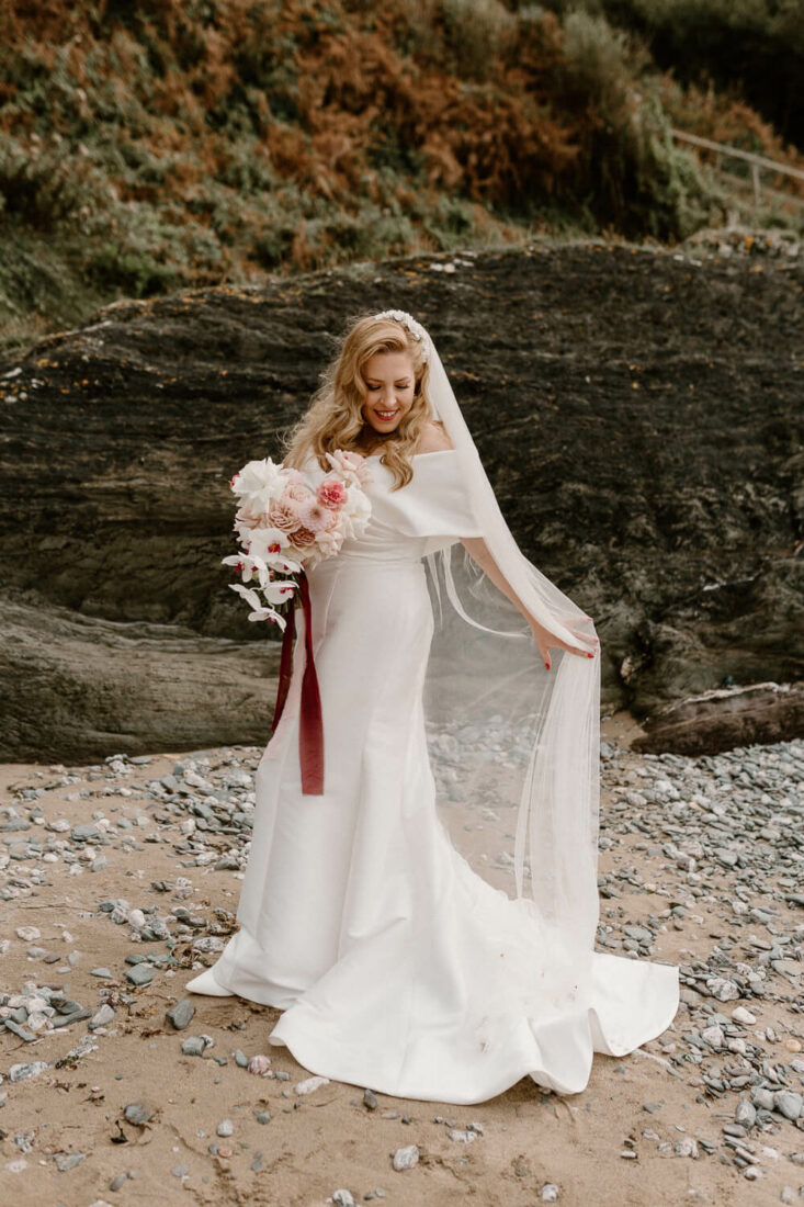 Bride adjusts veil on beach at Polhawn Fort Wedding in Cornwall.
